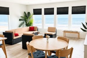 Ein modernes Wohnzimmer mit einem großen Fenster mit Meerblick, einem runden Holztisch und bequemen Sitzmöglichkeiten.