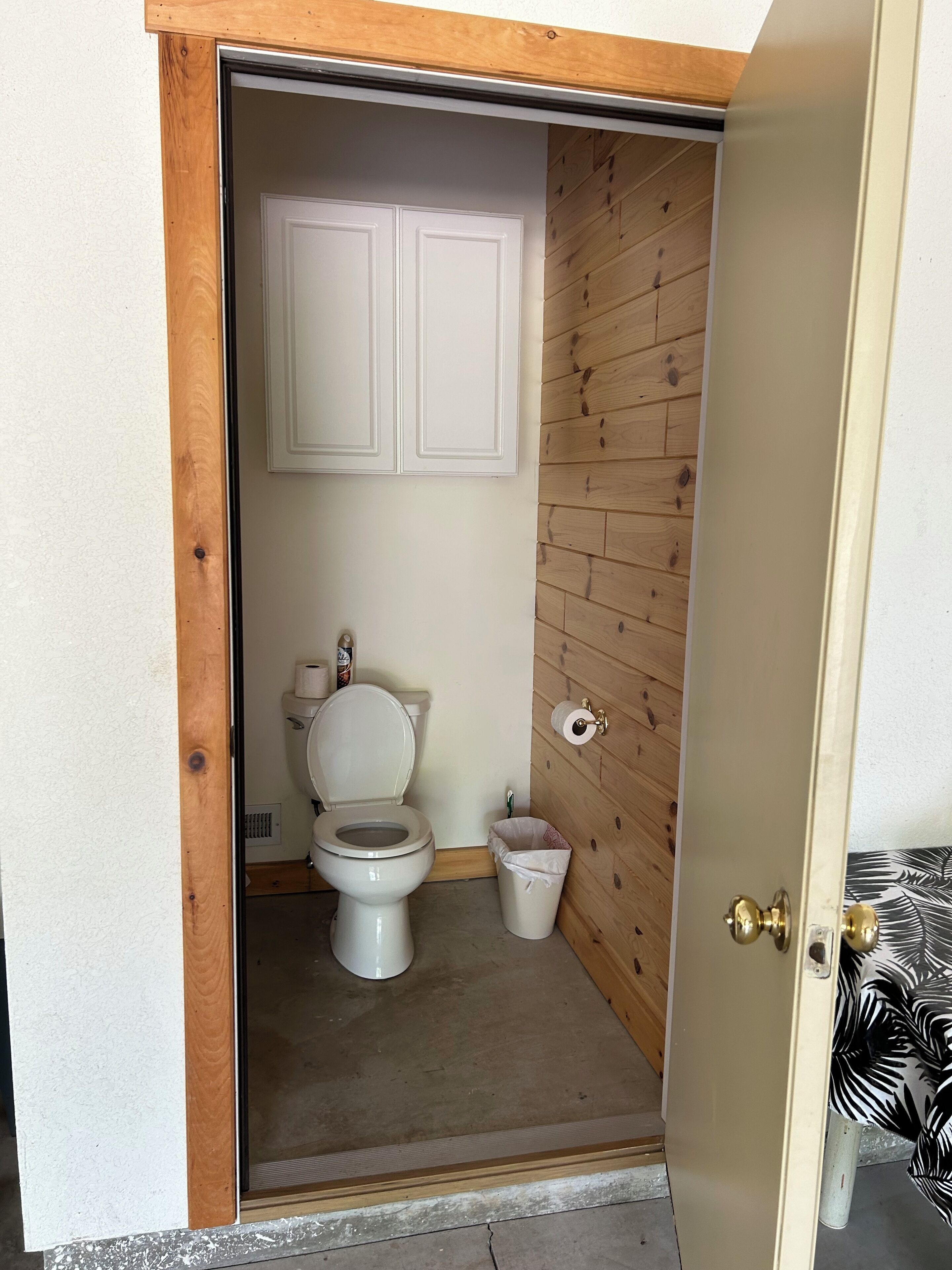 Un baño pequeño y funcional con pared de madera, inodoro y cubo de basura.