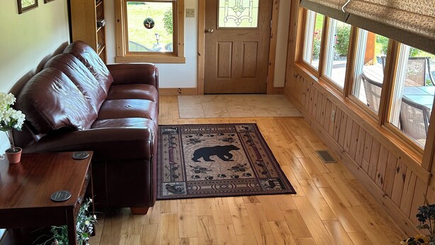 Een woonkamer met een bruine leren bank, een houten salontafel, een vloerkleed met een berendesign, en een houten deur met een glas-in-loodraam.