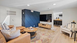 A modern living room with a sofa, coffee table, and a TV. There's a kitchen area in the background with a dining table and chairs. - Modern 2 Bed 1 Bath Walking Distance to Downtown (Brevard)