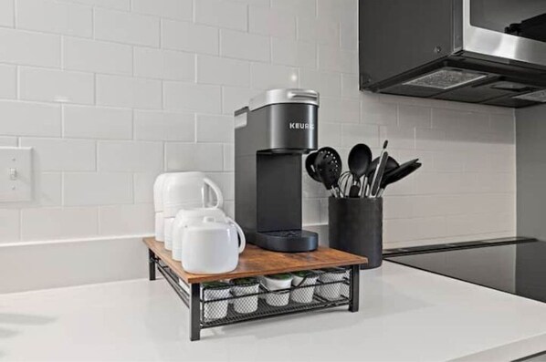 A modern kitchen with a coffee maker, a tray of white cups, and a utensil holder.