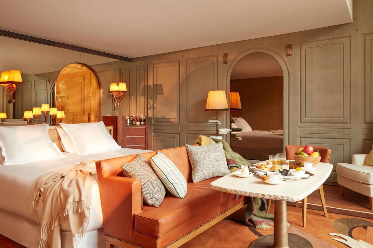 A hotel room with a bed, a sofa, a dining table with breakfast, and a mirror.