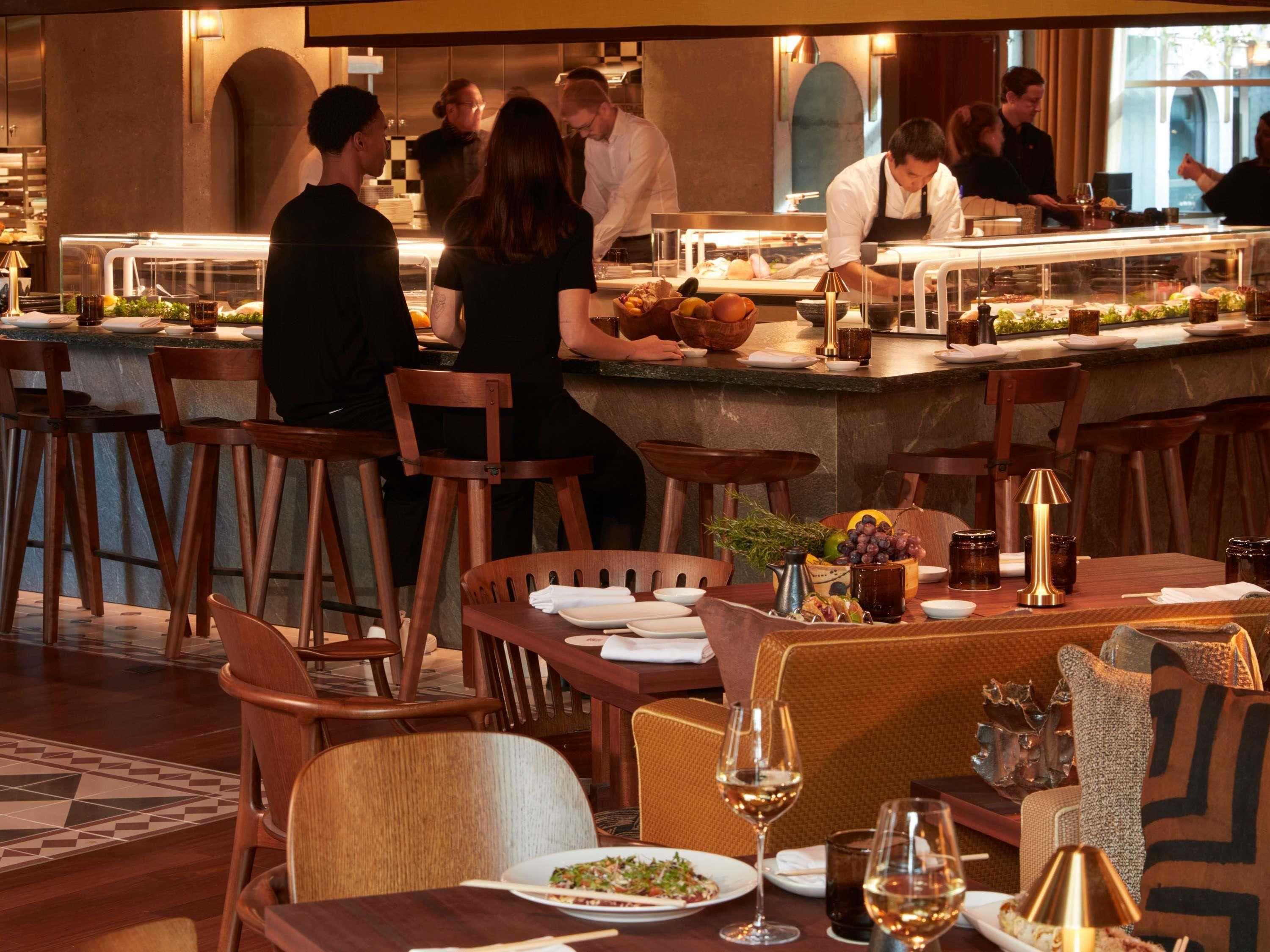 Un restaurant avec des chaises et des tables en bois, un coin bar et une vue sur la rue.