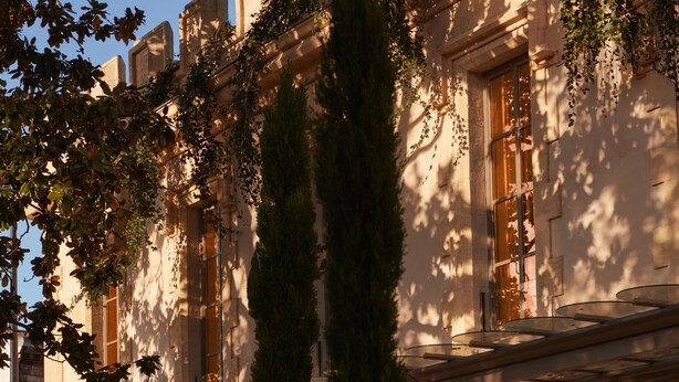 Un edificio histórico con altas ventanas, fachada de piedra y un jardín bien cuidado con un sendero.