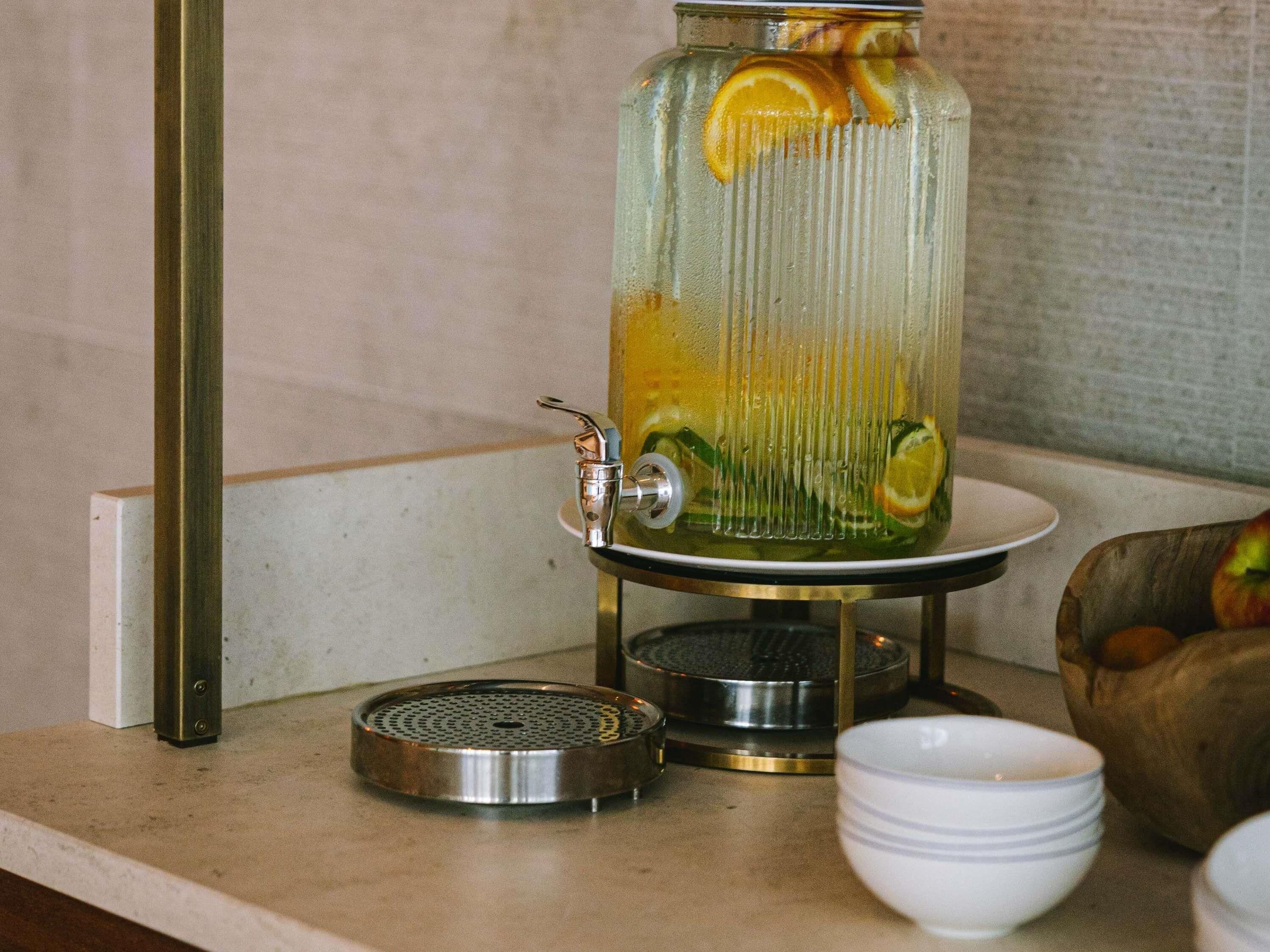 Un piano di lavoro in cucina con un recipiente in vetro contenente una bevanda, un colino in metallo e una ciotola.