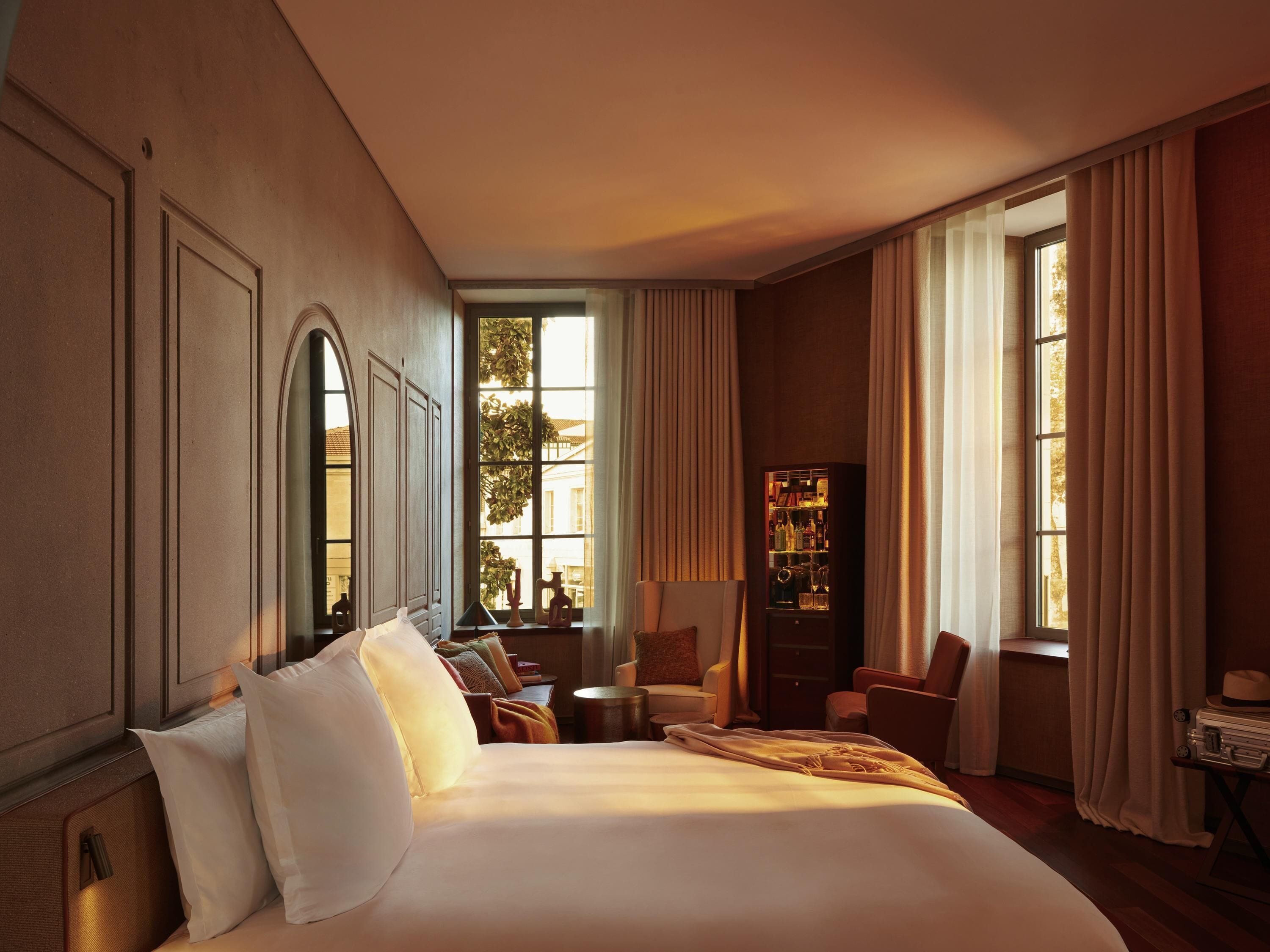 Una habitación de hotel con una cama grande, una zona de estar con sillas, una mesita y un mueble con botellas.