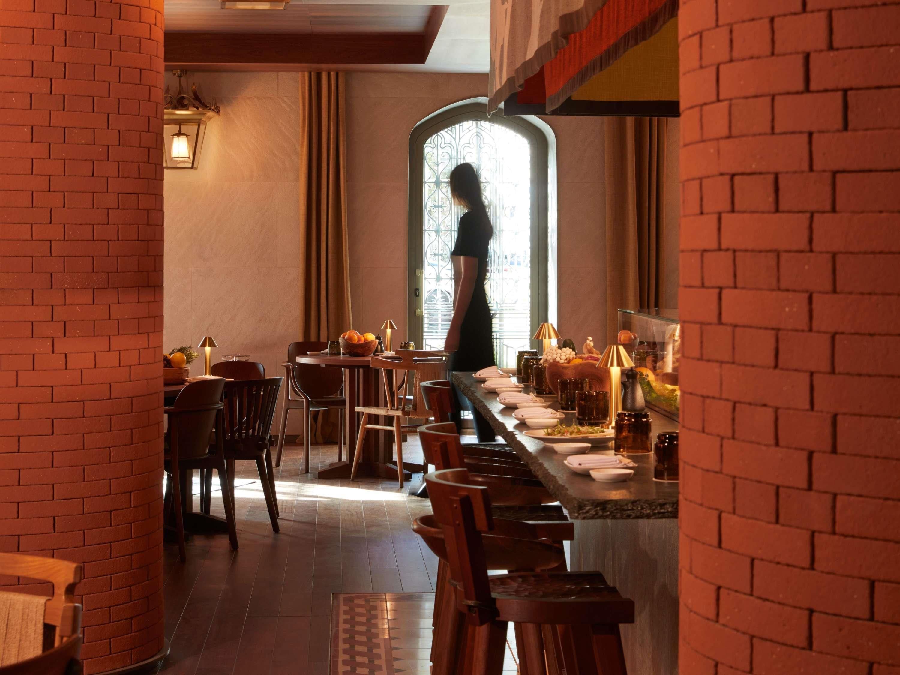 Un restaurante con paredes de ladrillo, una barra larga y una persona de pie junto a la ventana.