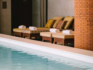 A poolside area with lounge chairs and towels, a brick wall, and a tiled floor. - Mondrian Bordeaux Les Carmes (Bordeaux)
