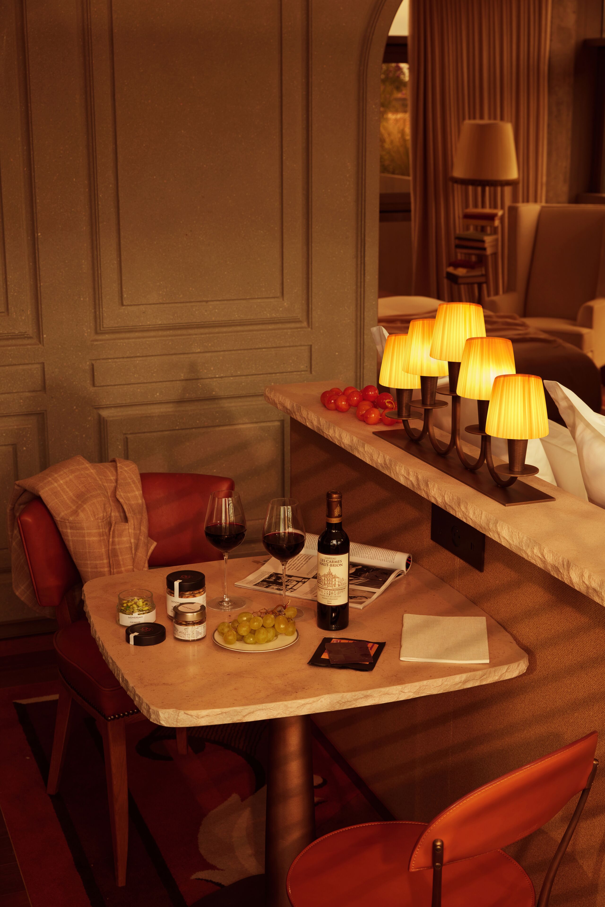 A dining area with a table set for two, featuring a bottle of wine, glasses, a plate of grapes, and a menu.
