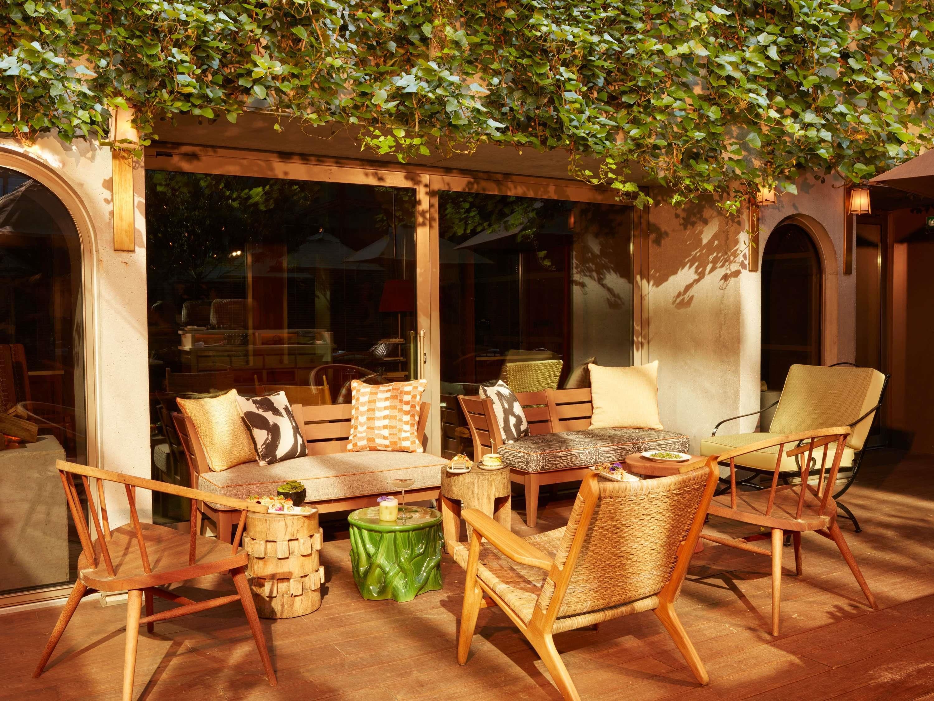 Un área de estar al aire libre con mobiliario de madera, una mesa verde y una pérgola cubierta de hiedra.