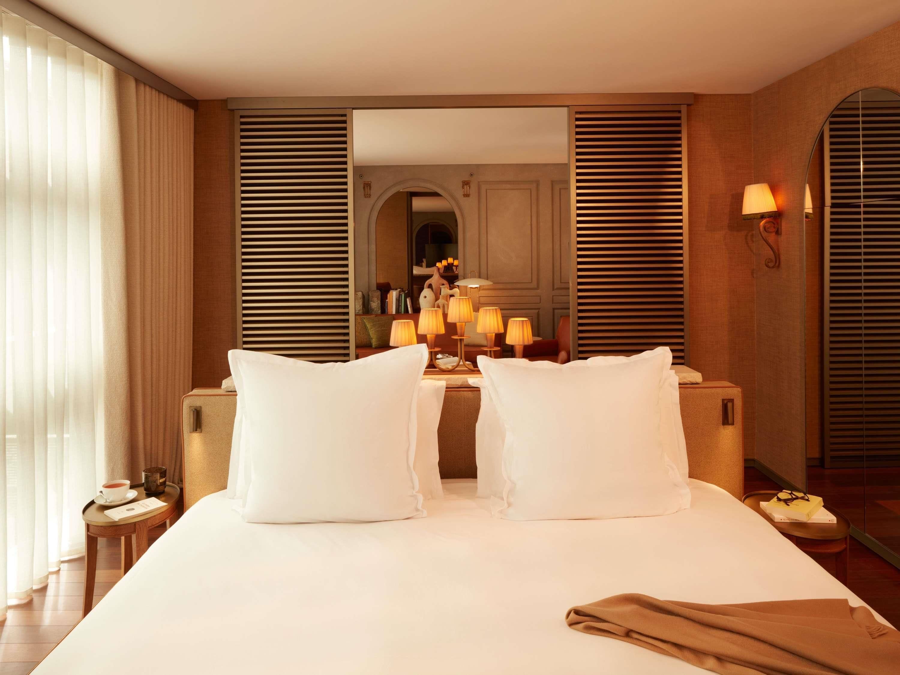 Een hotelkamer met een groot bed, twee nachtkastjes, een spiegel en een raam met gordijnen.