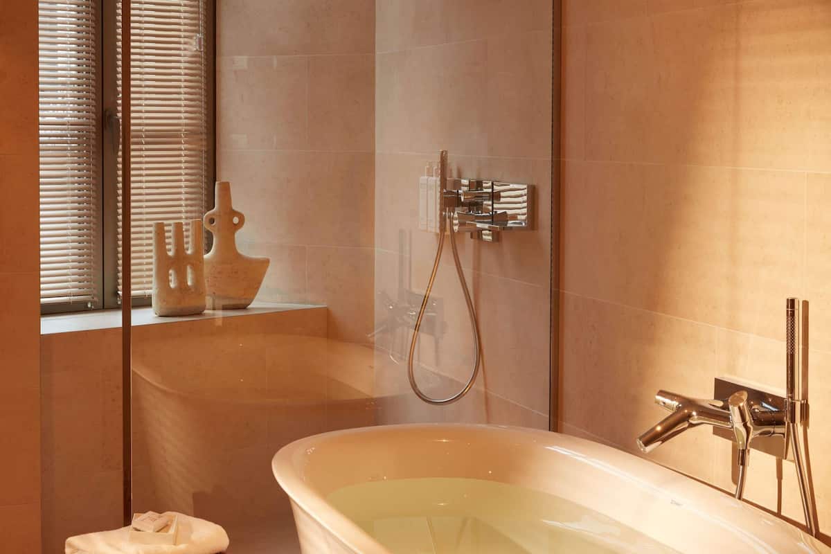 Un baño moderno con una bañera independiente, una ducha con cerramiento de vidrio y un taburete de madera con una toalla.