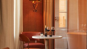 Habitación de hotel con una mesa redonda, dos sillas, una lámpara y vistas a través de un gran ventanal con persianas.