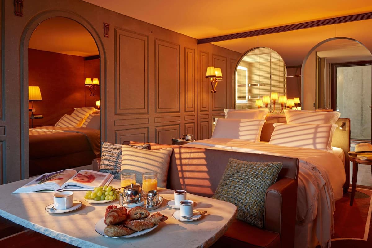 A hotel room with a large bed, a sitting area with a table set for breakfast, and a view through the window.