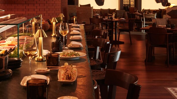Un restaurante con una barra larga, sillas de madera y mesas dispuestas para comer.