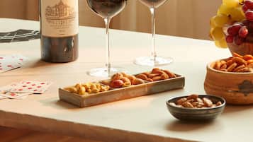A bottle of wine, two glasses of wine, a bowl of grapes, and a tray of snacks on a table.