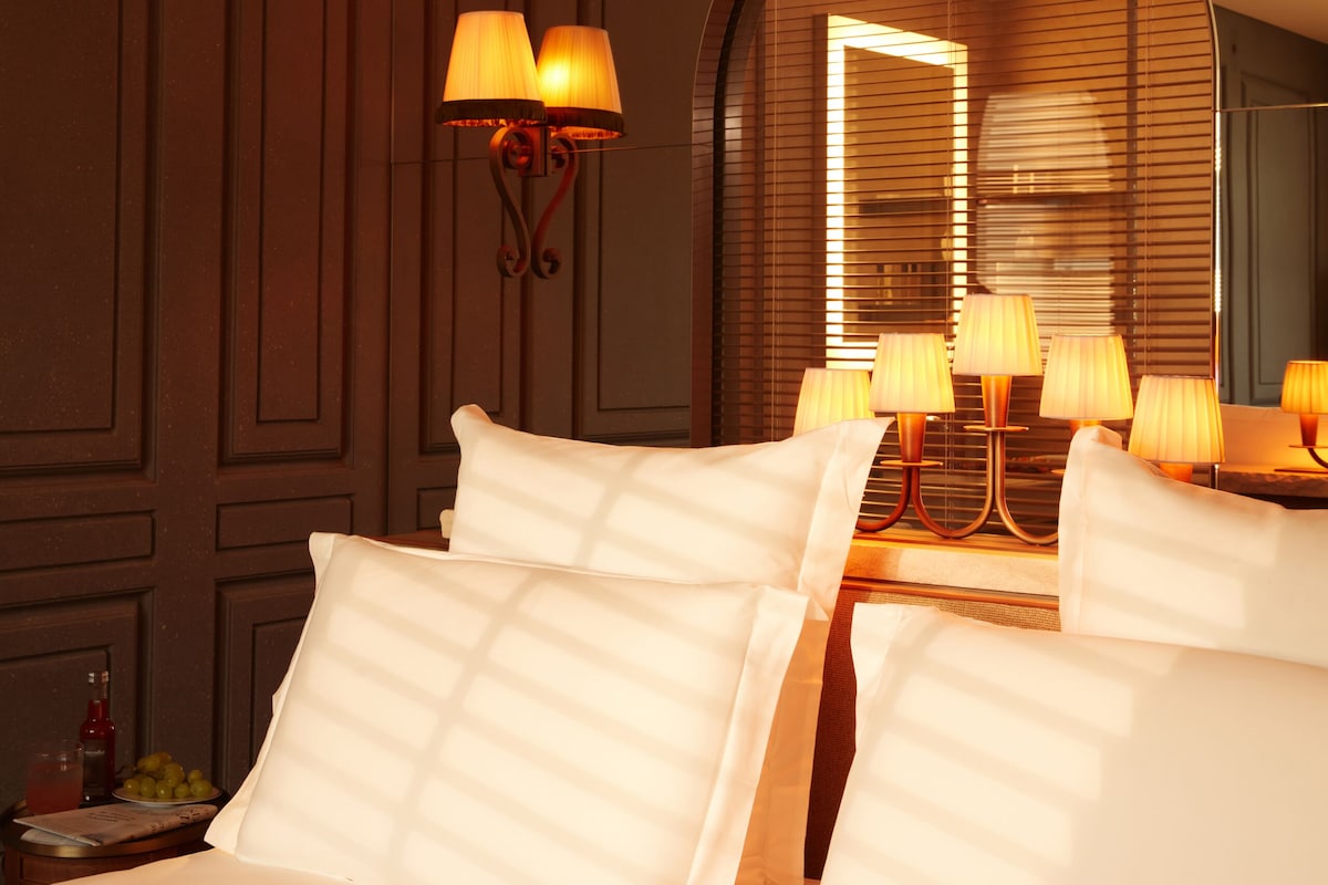 Habitación de hotel con una cama grande, varias lámparas, un espejo y un diseño de panel en la pared.