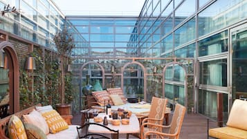 A glass-enclosed patio with seating, a table, and decorative items.