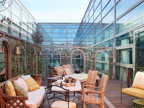 Ein wintergartenartiger Raum mit Sitzgelegenheiten, einem Tisch und Dekorationselementen.
