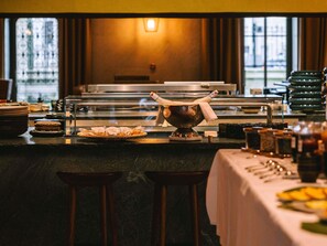 A buffet setup with a variety of food items, a decorative bowl, and a bar area with stools. - Mondrian Bordeaux Les Carmes (Bordeaux)