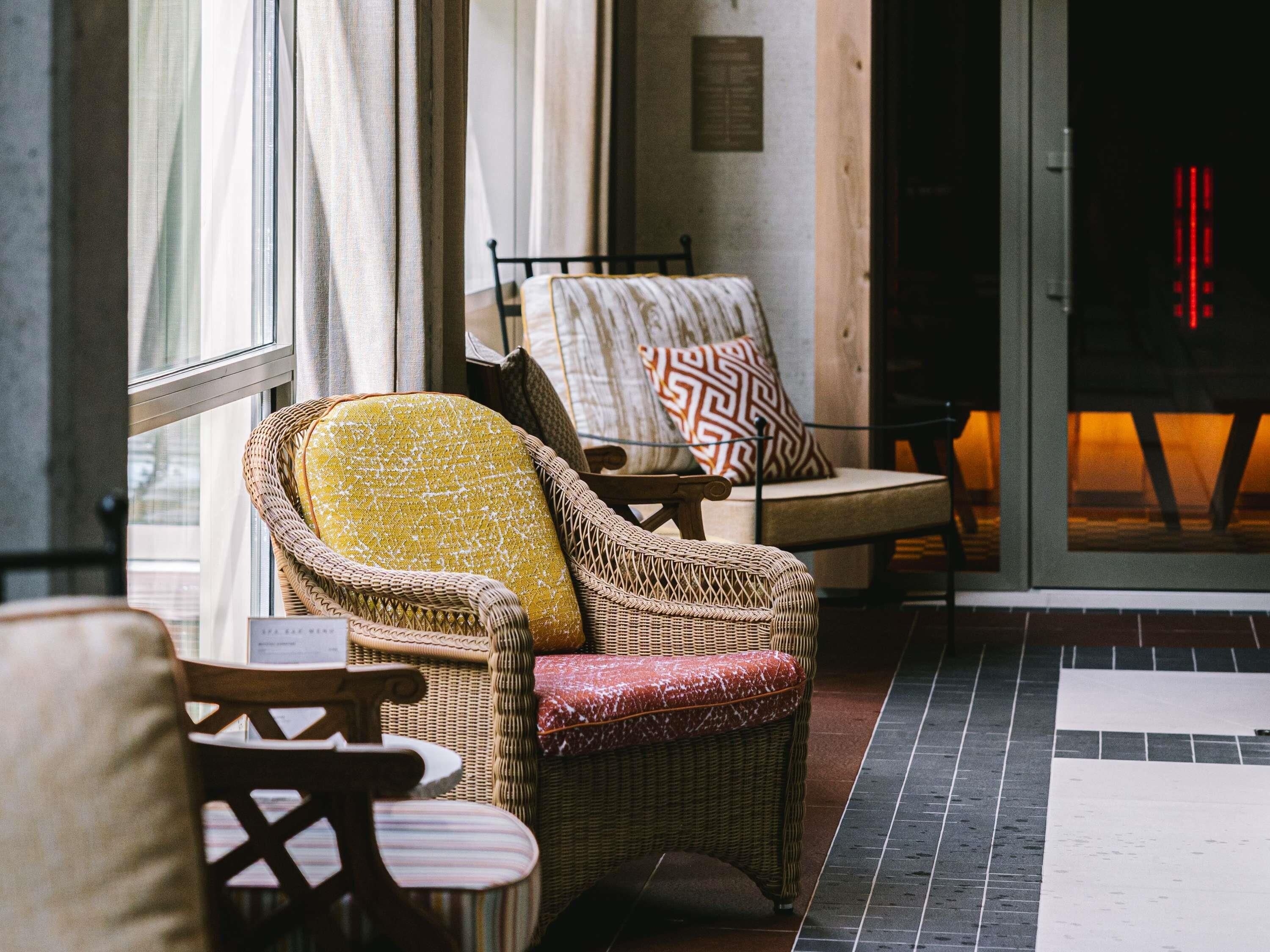 Wicker chairs with cushions, a small table, and a tiled floor in a room with a window and a door.
