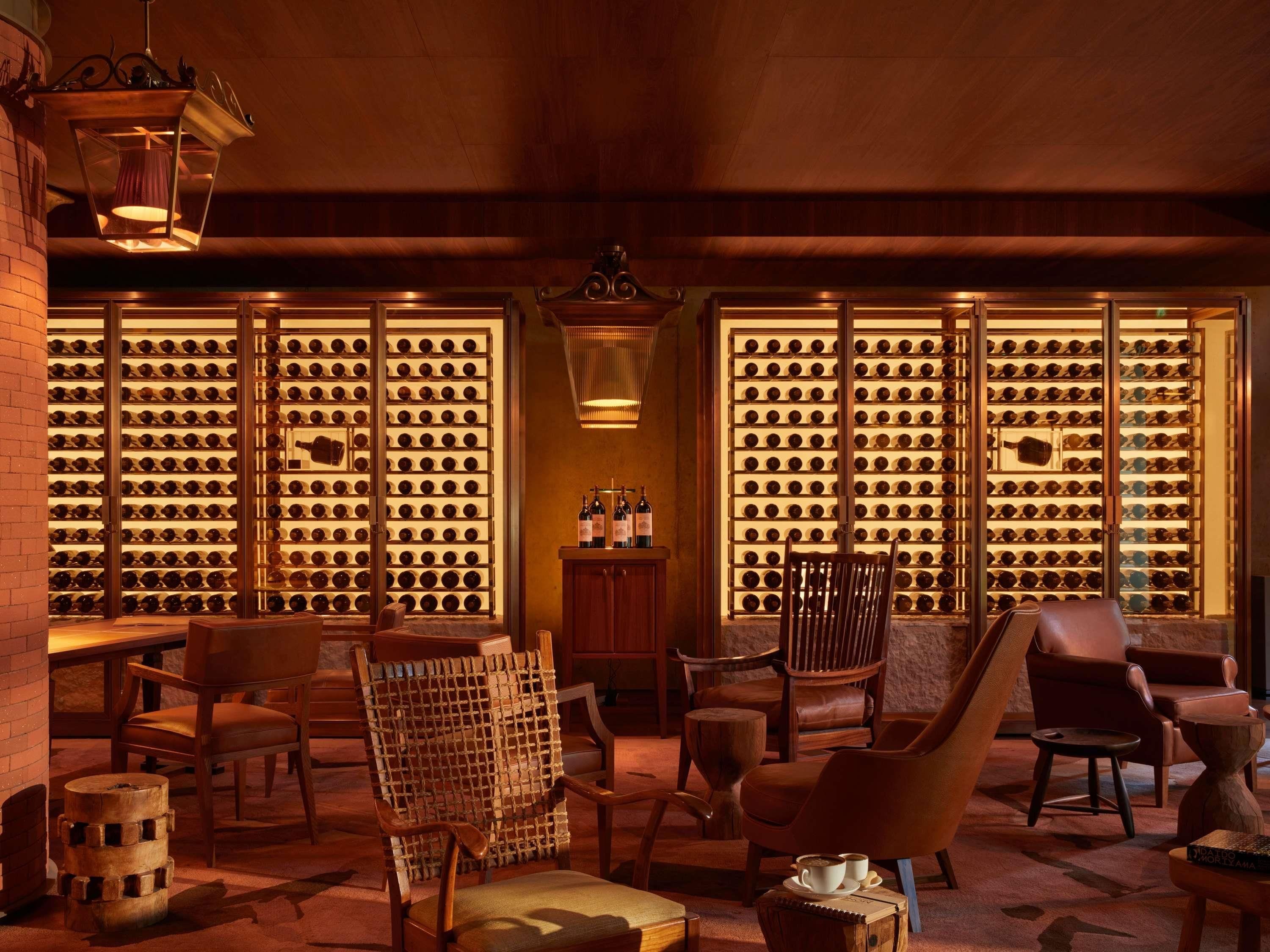 A wine cellar with wooden racks of wine bottles, leather chairs, and a wooden table with a bottle and glasses.