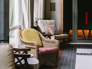 Wicker chairs with cushions, a small table, and a tiled floor in a room with a window and a door.