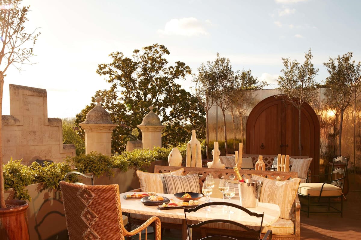 An outdoor dining area with a table set for two, surrounded by wicker chairs and a cushioned bench.