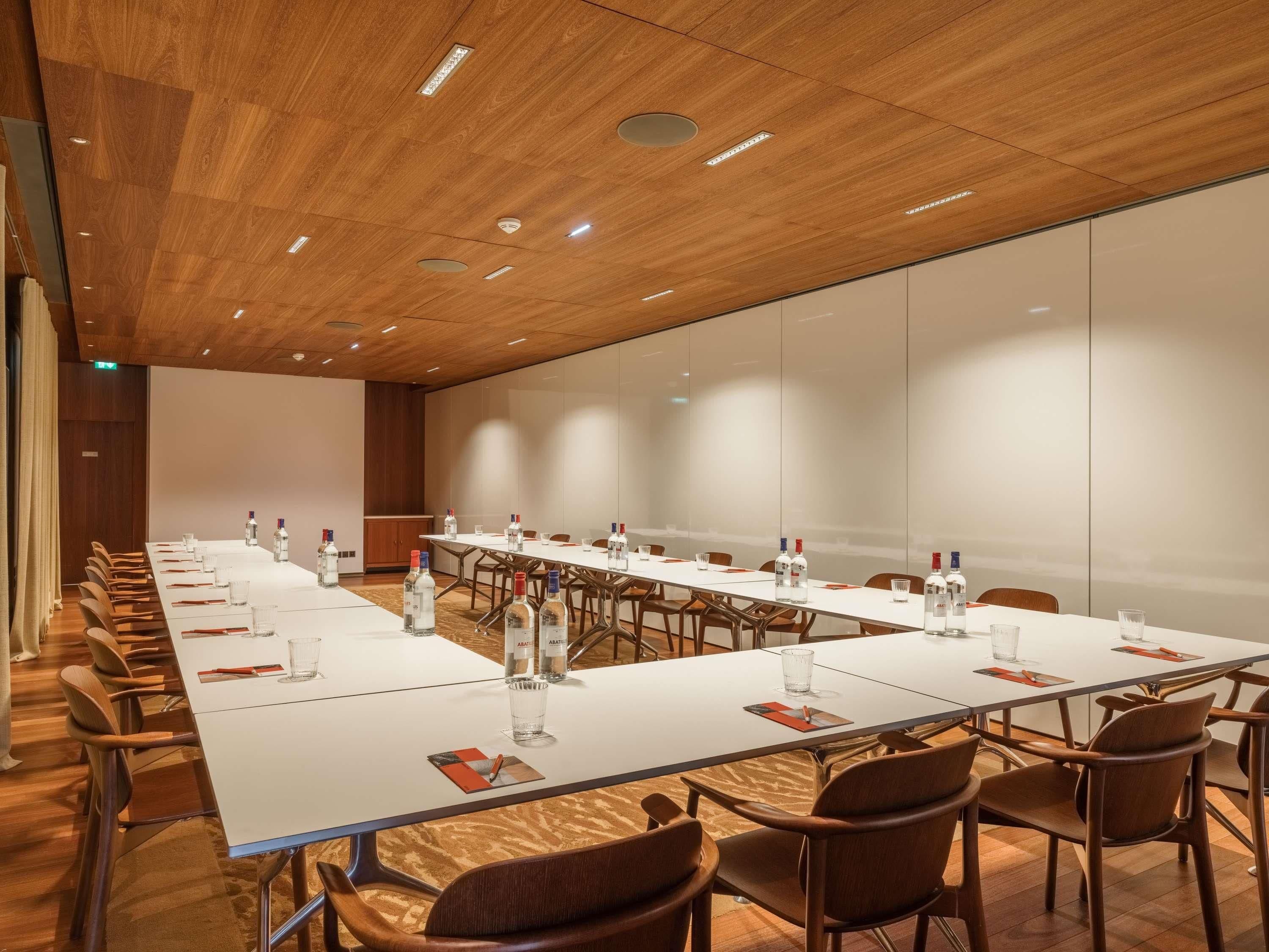 Un salón de conferencias con una larga mesa, sillas y botellas de agua.