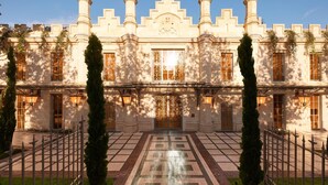 Un edificio imponente de arquitectura simétrica, con altas columnas, ventanas ornamentadas y una entrada central con un portón decorativo.