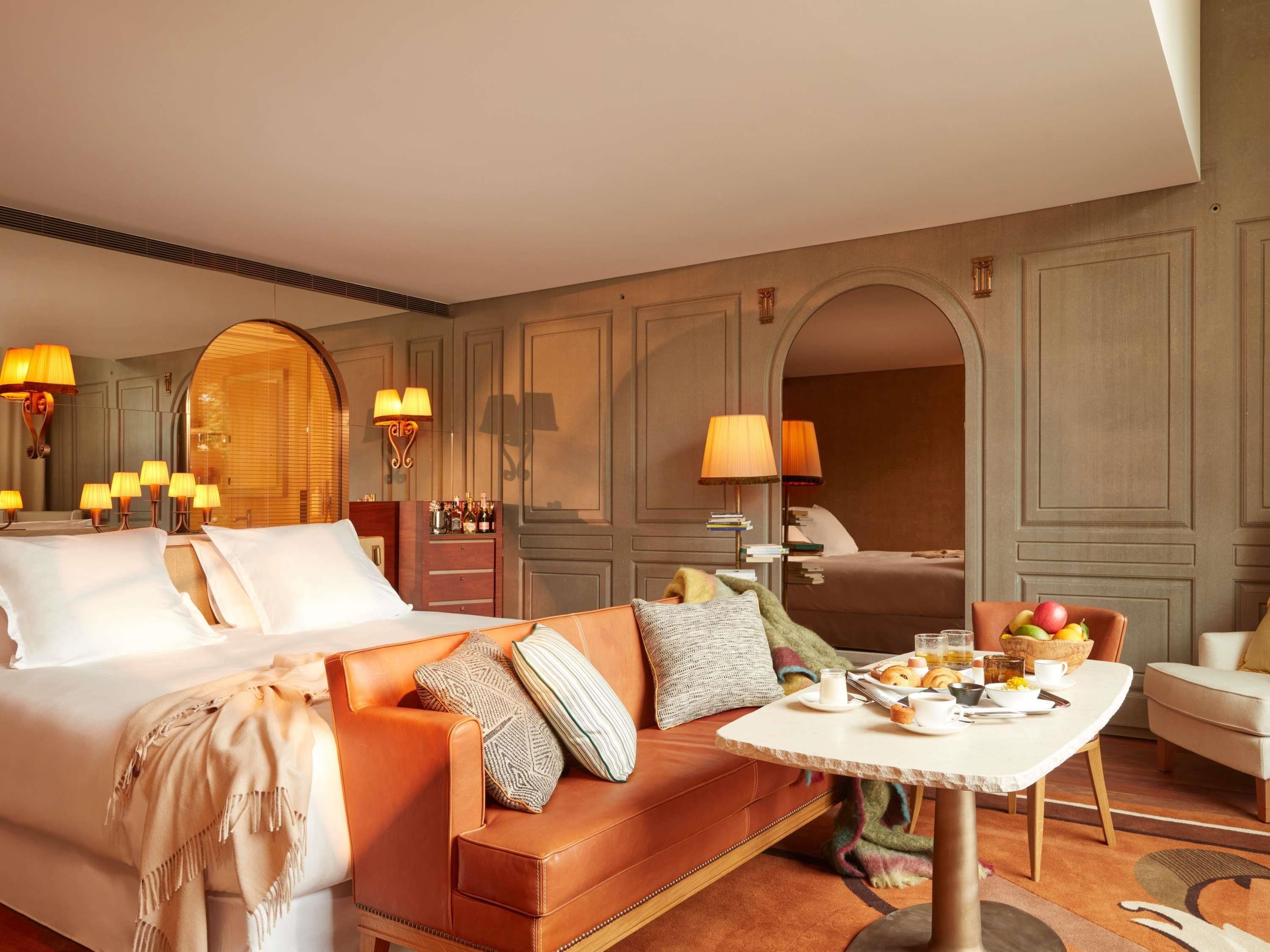 Una habitación de hotel con cama, sofá, mesa de comedor y desayuno, y un espejo.