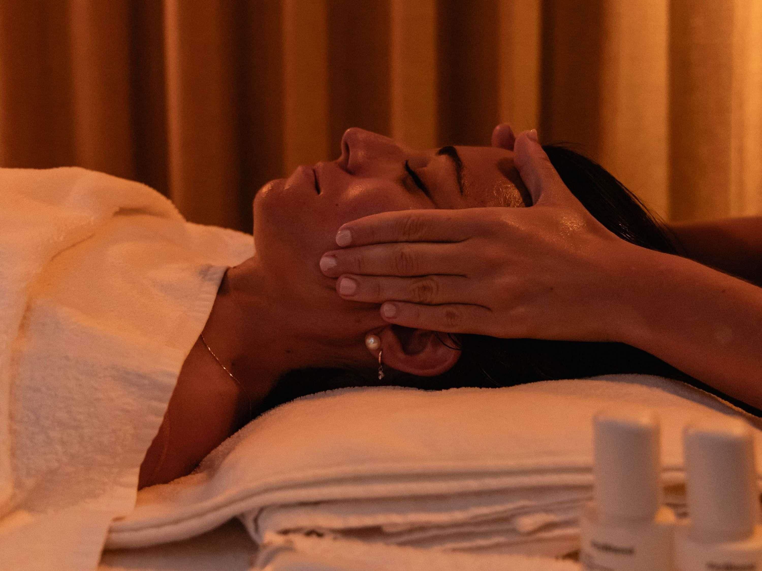 Une personne allongée, une main sur le visage, peut-être en train de recevoir un soin du visage.