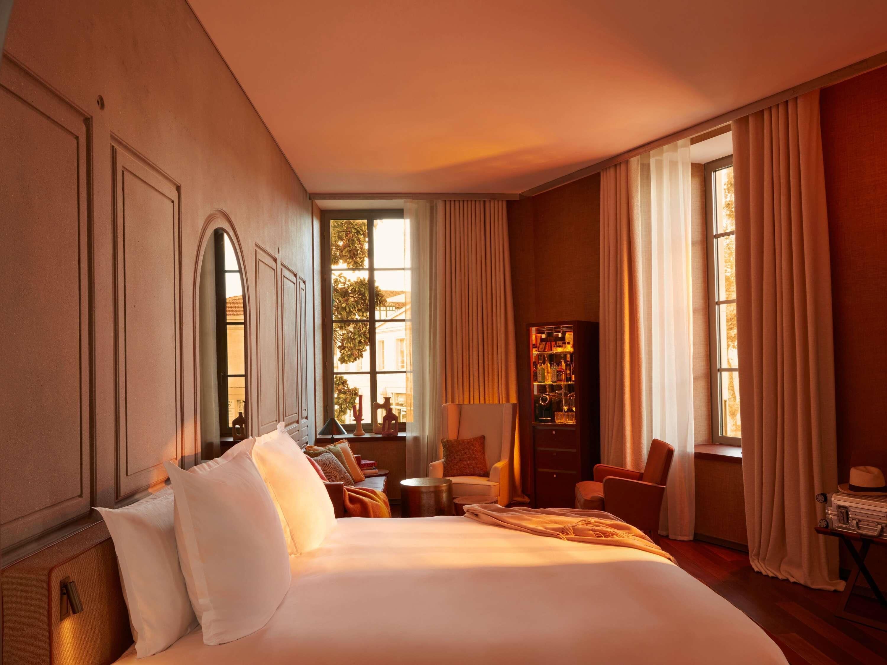 A hotel room with a large bed, a seating area with chairs, a small table, and a minibar.