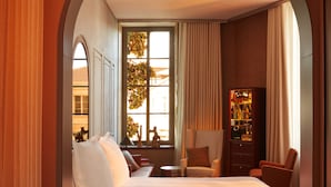 A hotel room with a large bed, a sitting area with a chair and a small table, a bookshelf, and a window with curtains. - Mondrian Bordeaux Les Carmes (Bordeaux)