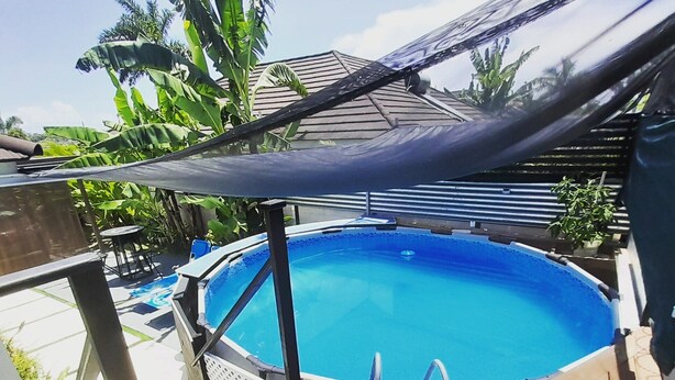 An outdoor swimming pool with a wooden deck, surrounded by tropical plants and a shaded area. - Near Dunn's River Falls, w/Pool, Beach Access, A/C, WiFi, Playpen & baby bath (Ocho Rios)