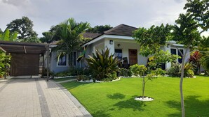 A residential property with a paved driveway, a covered carport, and a well-maintained lawn with various plants. - Near Dunn's River Falls, w/Pool, Beach Access, A/C, WiFi, Playpen & baby bath (Ocho Rios)