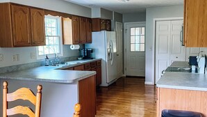 A kitchen with wooden cabinets, a refrigerator, and a dining area with chairs. - Cozy ranch style home close to Virginia Spearhead and Hatfield McCoy Trailheads  (Pocahontas)