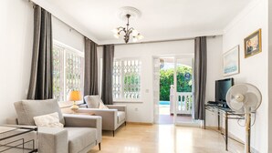 Un salon moderne comprenant un ensemble de canapés, un téléviseur, un ventilateur et une vue sur un jardin, visible à travers la porte vitrée.