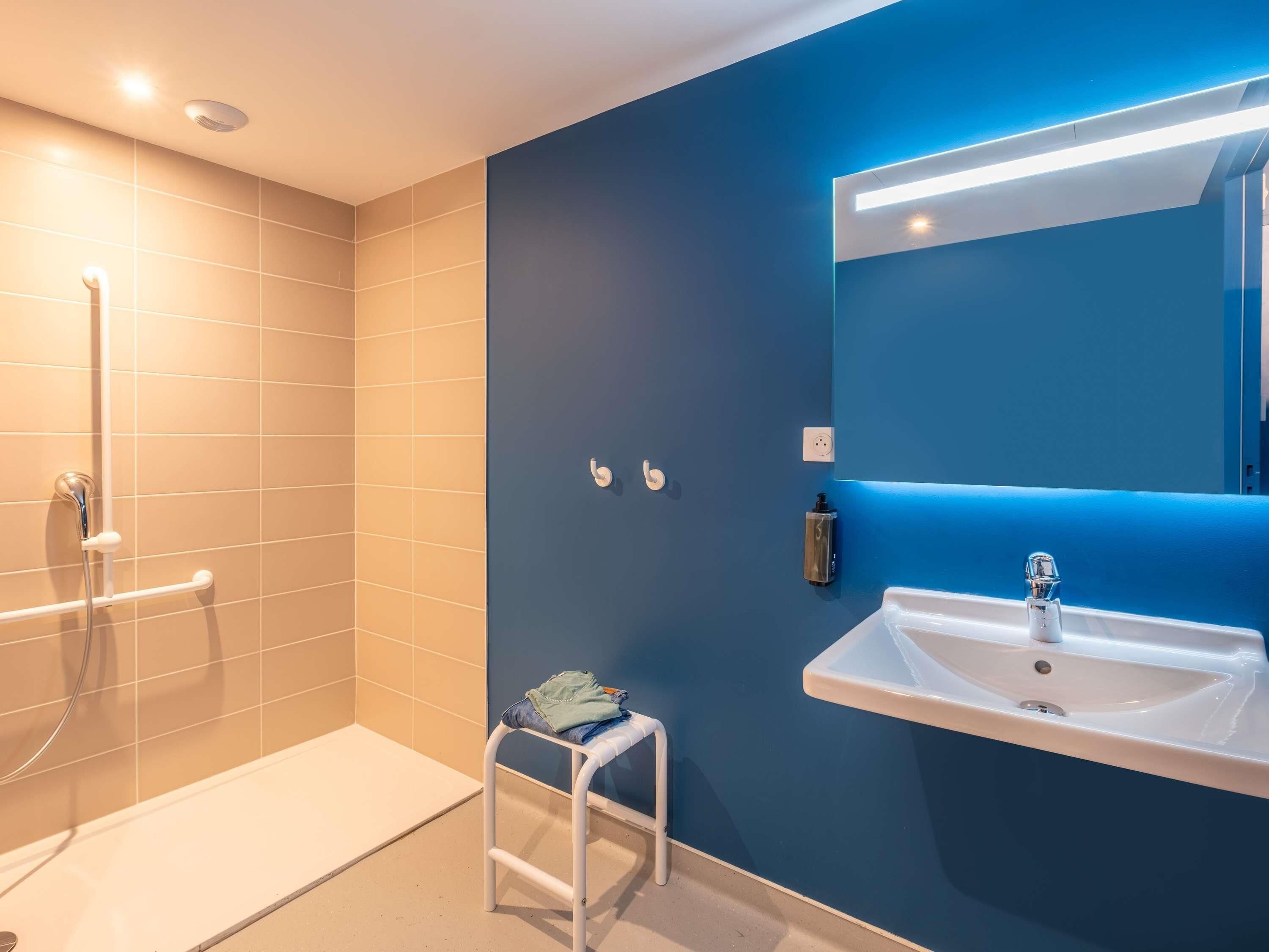 Un baño moderno con ducha, lavamanos y un taburete pequeño.