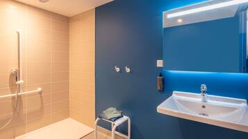 Un baño moderno con ducha, lavamanos y un taburete pequeño.