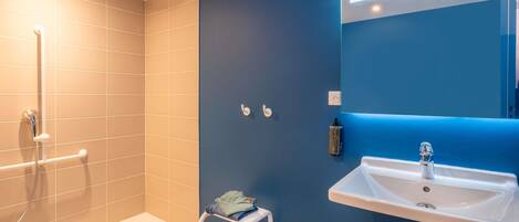 A modern bathroom with a shower, a sink, and a small stool.