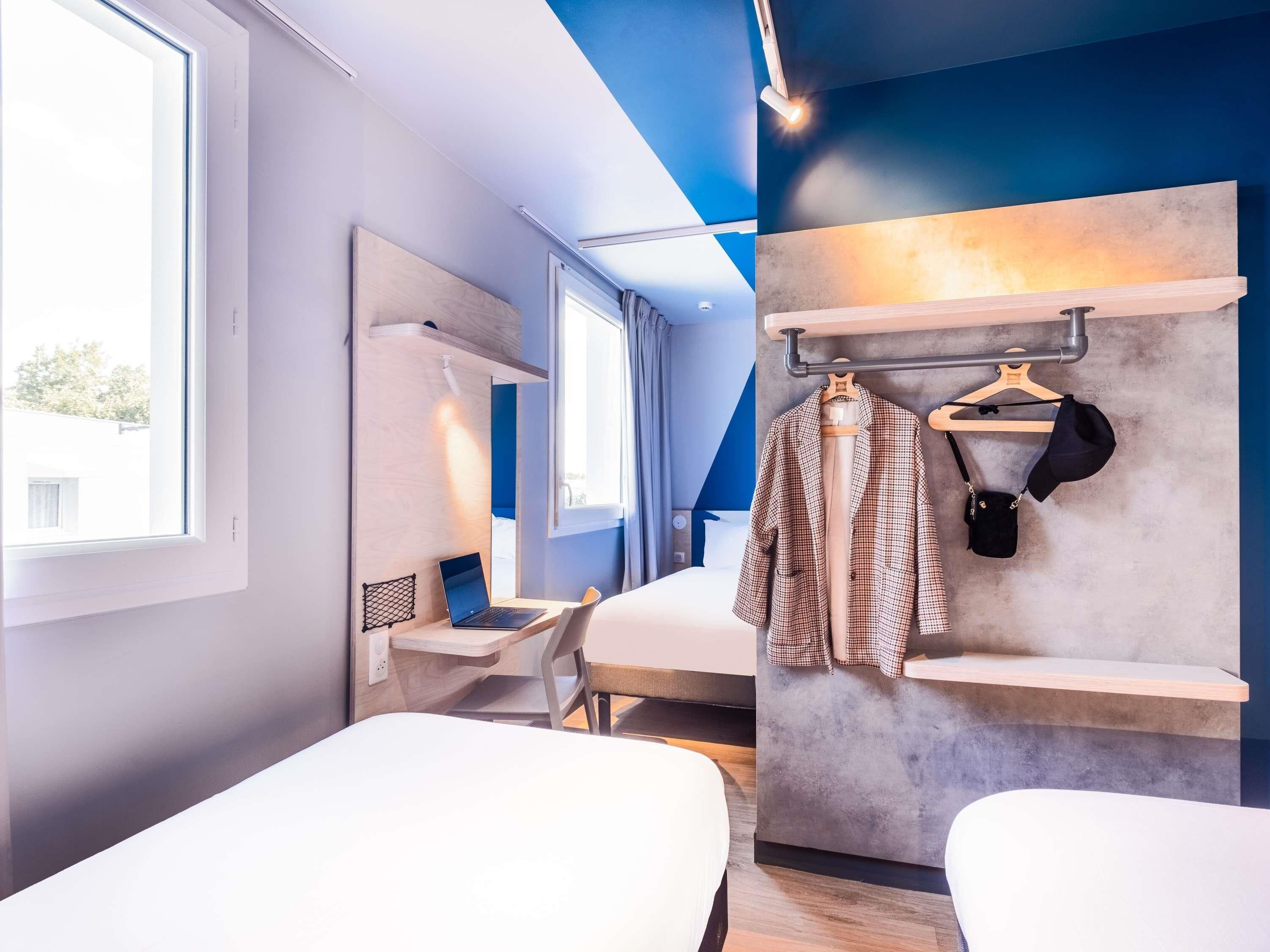Une chambre d’hôtel moderne équipée de deux lits, d’un bureau, d’une chaise, d’une armoire et d’un porte-manteau.