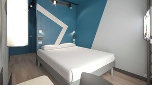 A modern hotel room with a bed, a desk, and a chair. - Ibis Budget Nantes Nord Treillières (Treillieres)