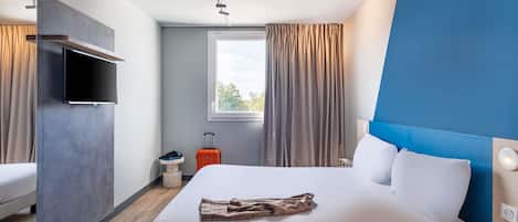 Una habitación de hotel moderna con cama, televisión, ventana con cortinas y maleta.