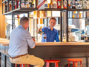 Baaritiski, jossa baarimikko kaataa juomia, hyllyt täynnä alkoholijuomapulloja ja kyltti, jossa ilmoitetaan, että paikalla on alkoholilupa.