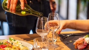 A person pouring a clear liquid from a green bottle into a glass on a table with a plate of food and another glass. - Ibis Budget Nantes Nord Treillières (Treillieres)
