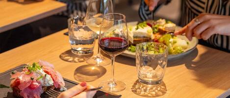 Una mesa de comedor con platos de comida, vasos de agua y vino, y una persona usando un tenedor.