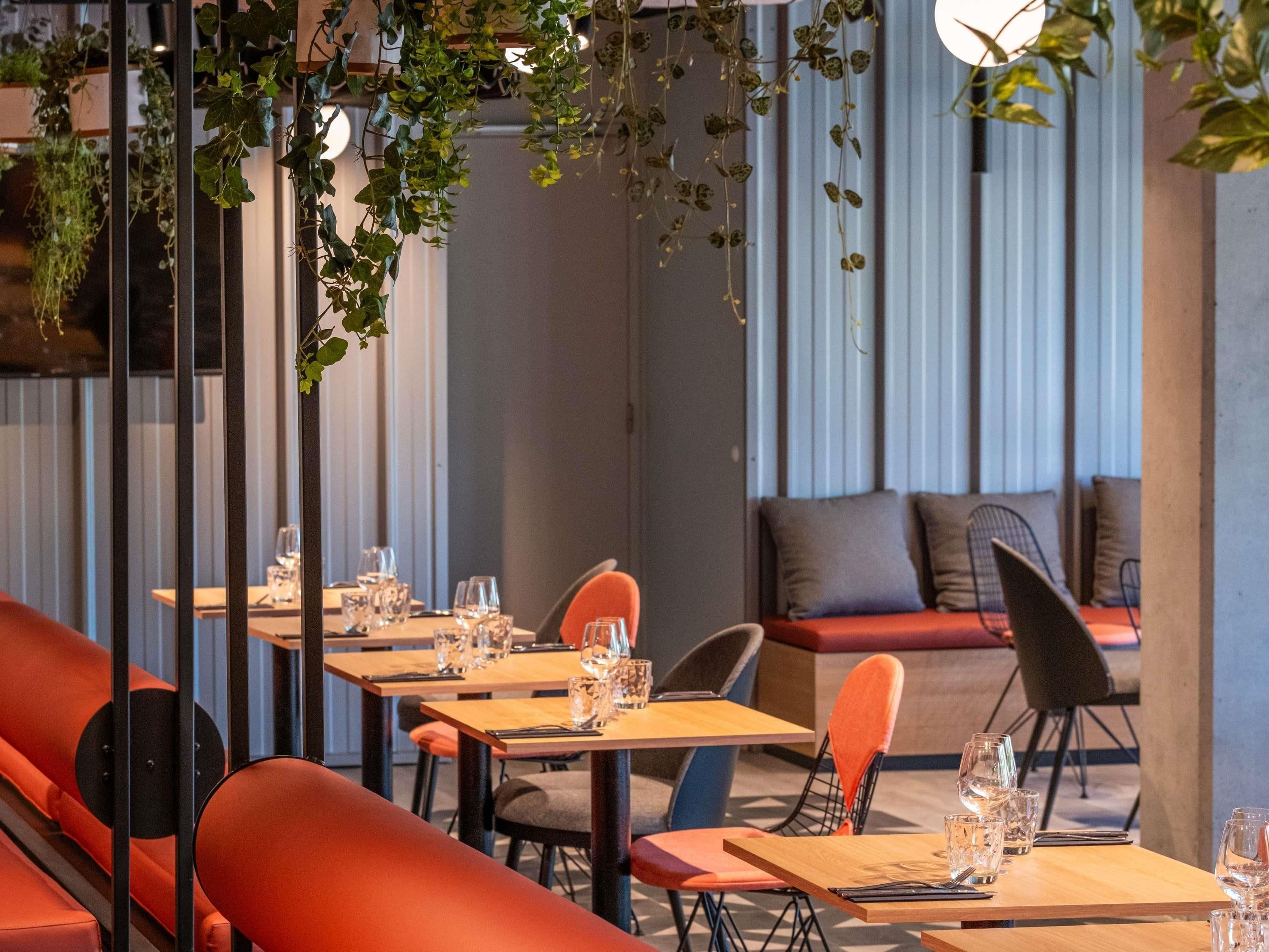 Un restaurante con mesas de madera, sillas anaranjadas y plantas colgantes.