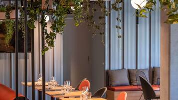 A restaurant with wooden tables, orange chairs, and hanging plants.