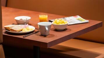 A breakfast setup with toast, eggs, a bowl of fruit, a cup, and a glass of orange juice on a table.